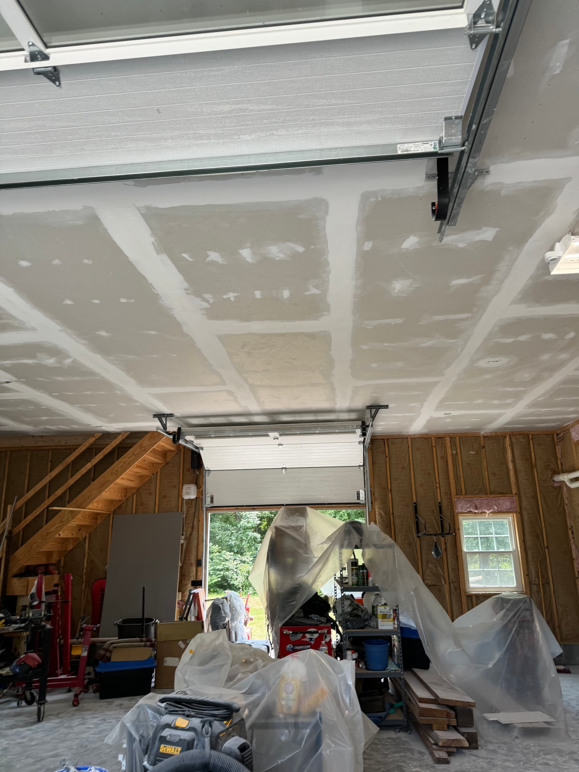 Garage ceiling drywall with finished seams and contents covered in plastic